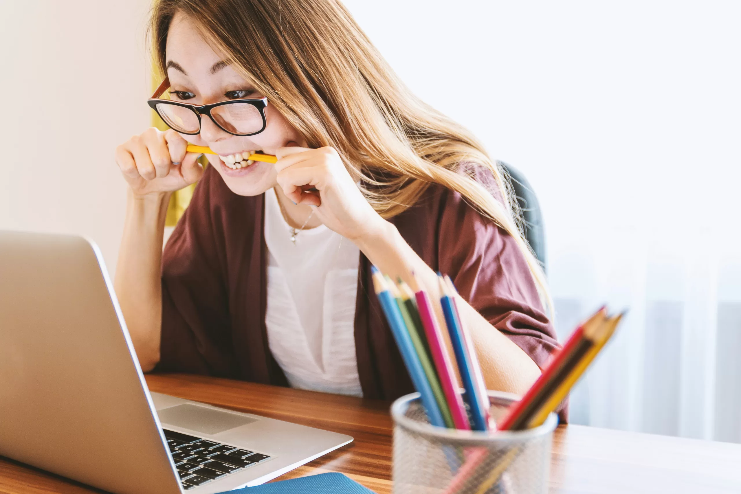 woman biting a pencil in anger while using a laptop